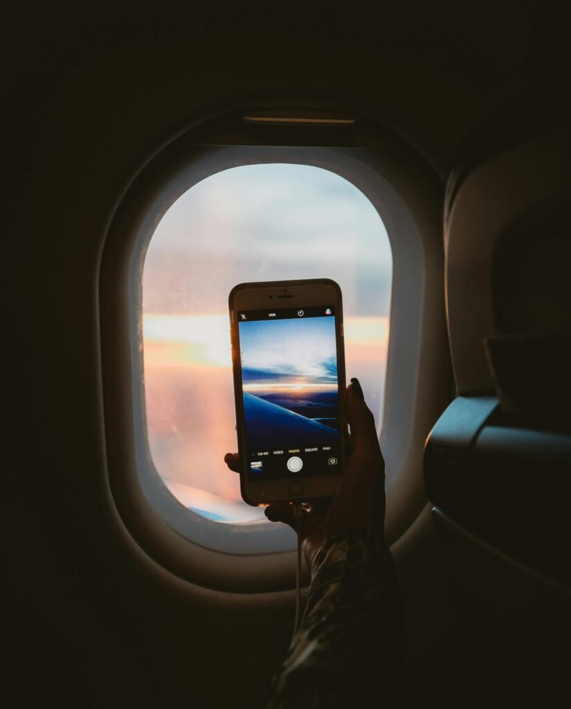 Our Amazon Travel Essentials A person takes a photo of a sunset through an airplane window using a smartphone.