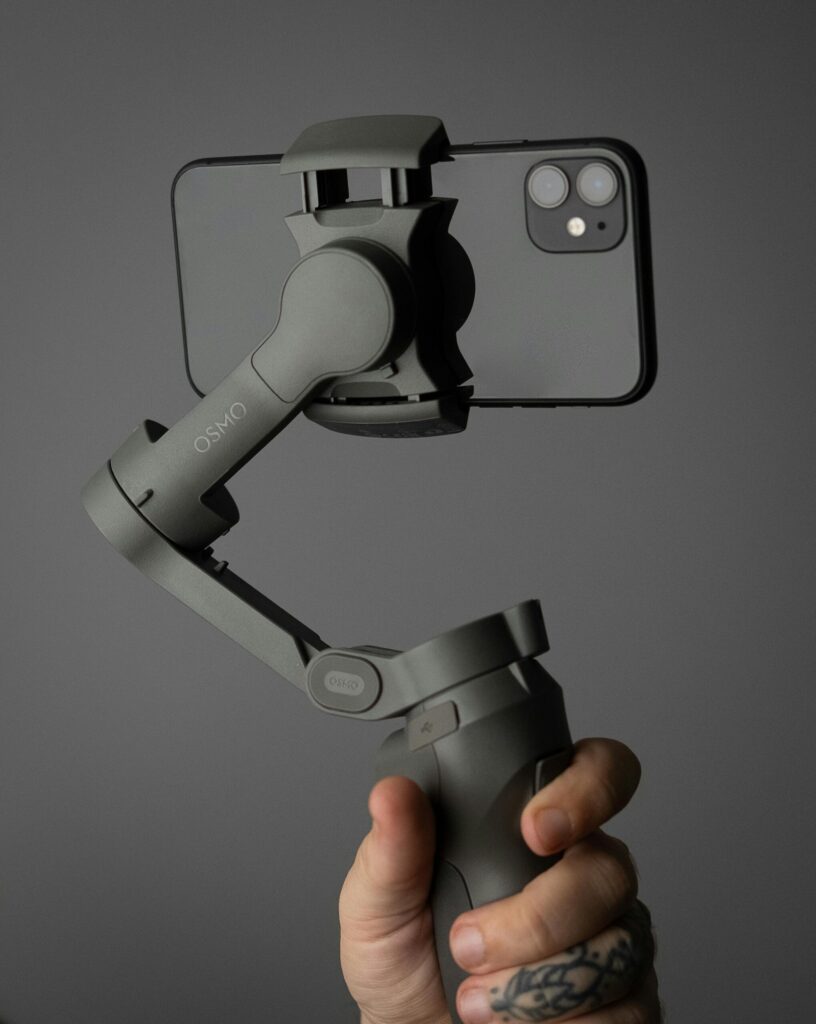 Our Amazon Travel Essentials Hand holding a smartphone mounted on a stabilizer against a solid background with tattooed fingers.