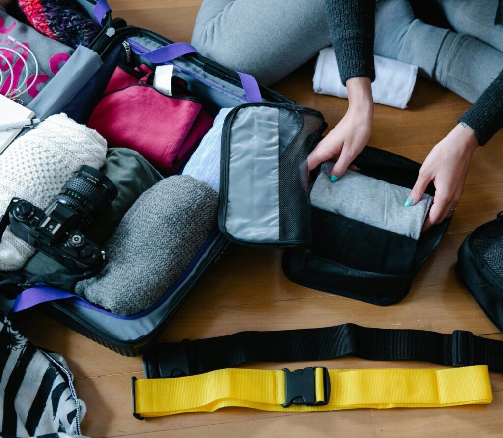 Our Amazon Travel Essentials A woman arranging clothes and accessories into a suitcase, preparing for travel.
